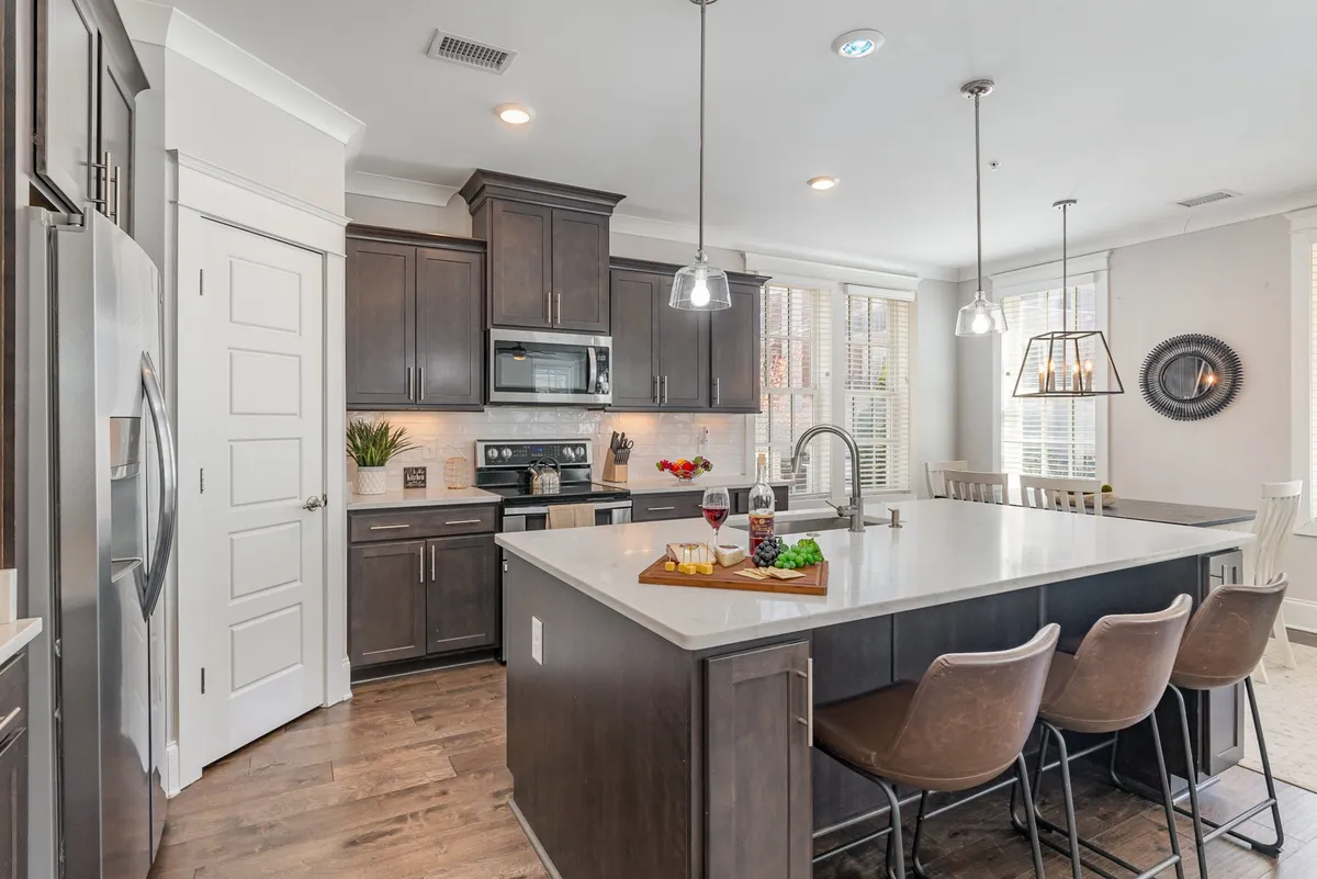 A bright, inviting kitchen with a central island, bar stools, modern appliances, and a cutting board with food, suggesting a fully equipped, welcoming space ready for meal preparation or social gatherings.