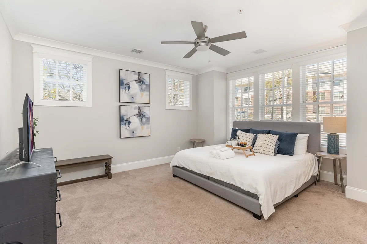 A quietly elegant bedroom with a plush bed, modern wall art, a sleek lamp, and a wall-mounted television. The bedding and decor create a calming, restful atmosphere, perfect for unwinding after a day out.