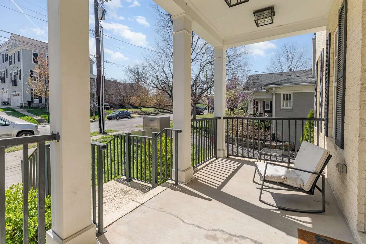 A welcoming front porch with a classic rocking chair set among lush greenery, offering a peaceful spot for relaxation and neighborhood views. The inviting setup showcases the quintessential Southern porch experience.