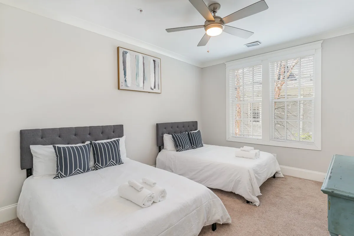 A welcoming bedroom with two beds adorned with striped pillows, artwork on the wall, and a window with blinds. The layout is perfect for families or groups, offering a relaxed and comfortable setting.