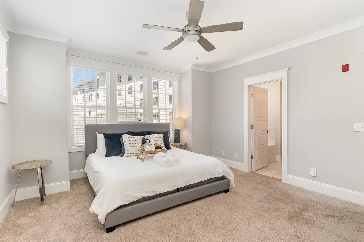 A sunlit bedroom with a comfortable bed, decorative pillows, a stylish nightstand, and a window streaming in natural light. The space feels serene and inviting, ideal for a restful retreat.
