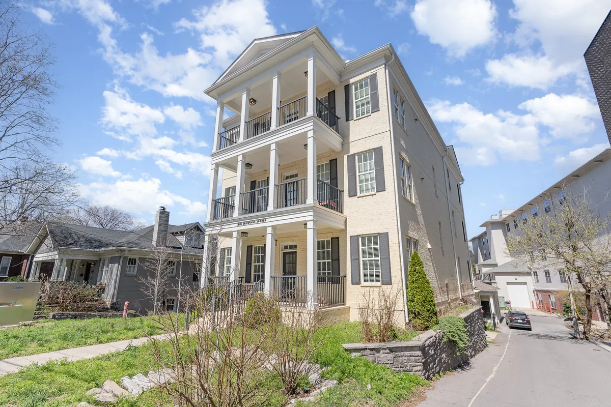 The image captures a large, welcoming front porch with comfortable seating, framed by a landscaped front yard and three stories of windows. The scene hints at a relaxing homecoming after a day of adventure, with plenty of space for family gatherings and morning coffee rituals.
