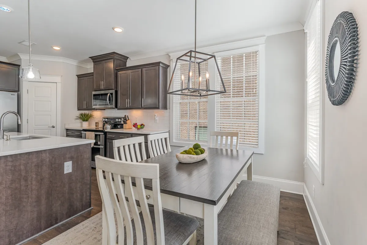 A welcoming dining area with a beautifully set table as the focal point, adjacent to a kitchen island and framed by large windows. The scene exudes hospitality, perfect for family meals, celebrations, or casual brunches in sunlit comfort.