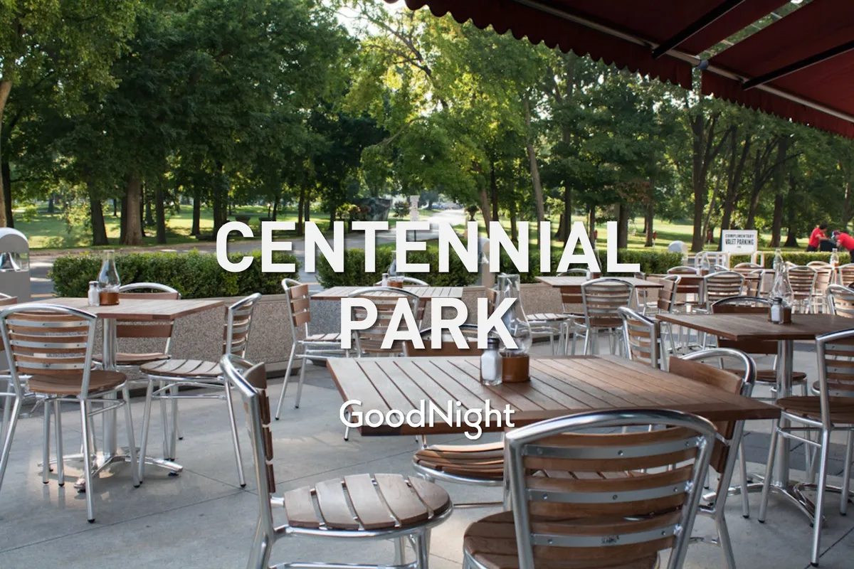 A cheerful park scene featuring outdoor seating under green trees, wooden tables along a park pathway, and people enjoying relaxed dining and social gatherings. The ambiance is inviting, with hints of sunset light, suggesting a perfect spot for al fresco meals or evening drinks.