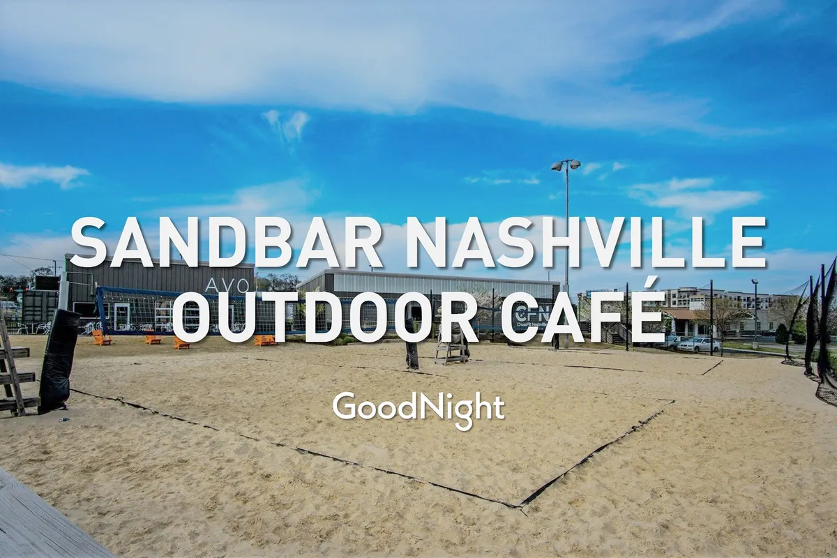 The scene features a lively sand volleyball court surrounded by outdoor café seating and modern buildings in the background. Groups of friends are seen playing volleyball, chatting, and enjoying food and drinks in a relaxed outdoor environment.
