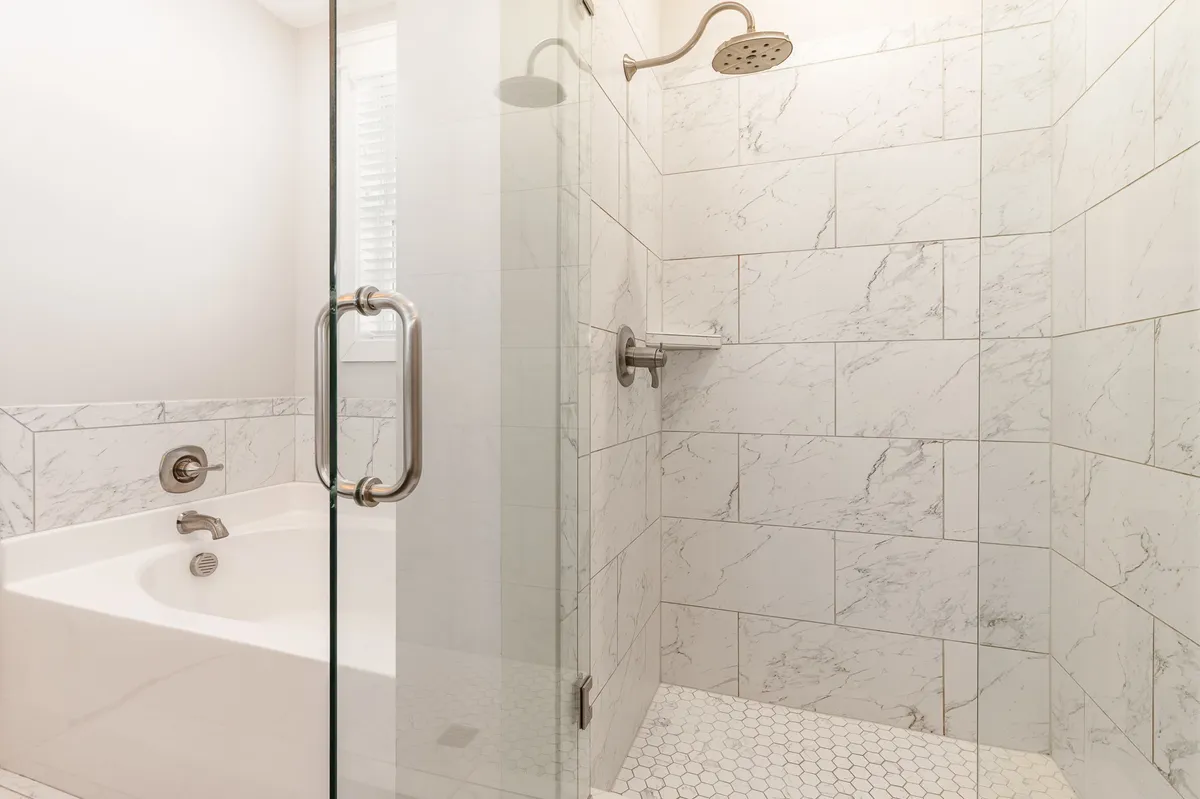 A modern bathroom featuring a glass-enclosed shower, a luxurious bathtub, and elegant marble tile. The space feels spa-like, inviting guests to unwind and recharge.
